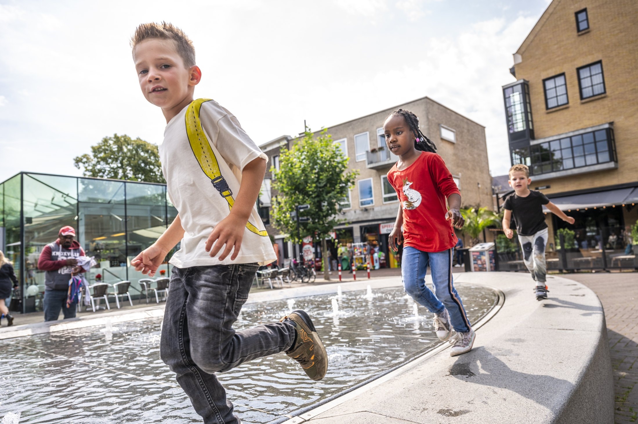 Kinderen rennen door de fonteinen op een plein met terrassen.