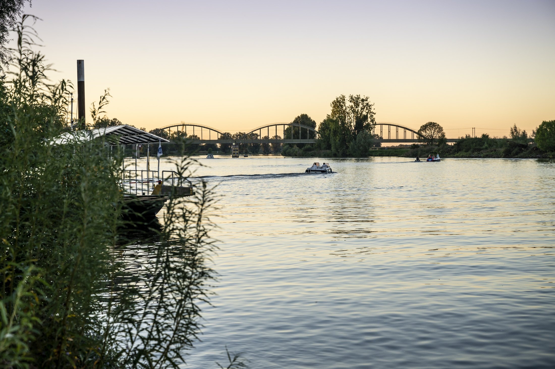 De Maas bij Ravenstein met een brug en boten in het avondlicht.